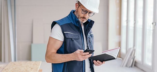 Afbeelding van een vakman met een mobiele telefoon en een notitieblok