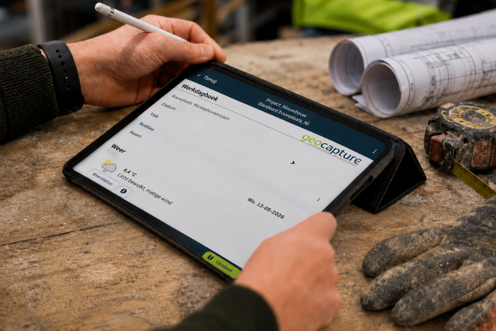 Ein Mitarbeiter bedient mit einem Eingabestift ein Tablet auf einer Werkbank. Auf dem Bildschirm ist eine geoCapture-Projektansicht mit Angaben zu Mitarbeitenden geöffnet; daneben liegen Baupläne, ein Maßband und Arbeitshandschuhe.